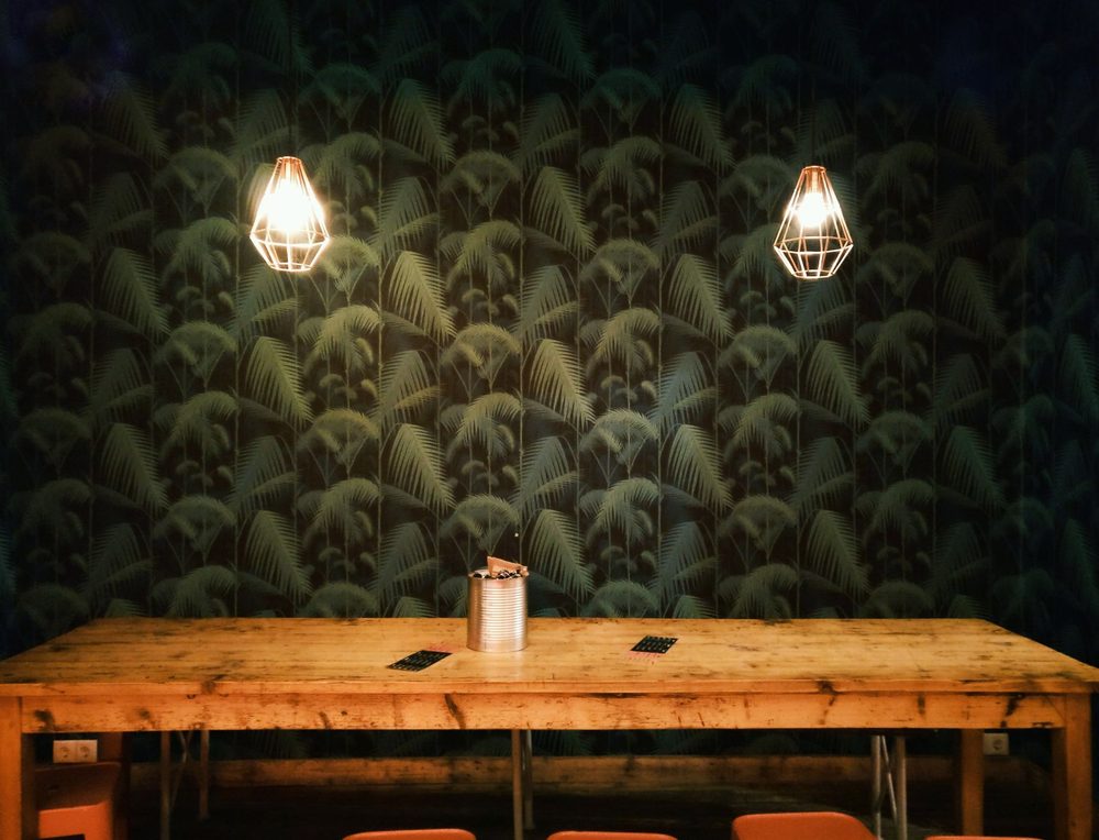 Dining room with a deep green palm-leaf wallpaper and rustic wood table