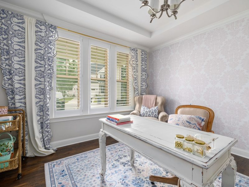 Room with a blue floral wallpaper accent wall and white writing desk